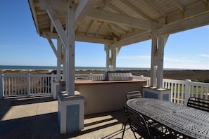A covered outdoor area with a table and chairs, a white fence, and a view of the ocean. - Sandy Turtle -Bayside-Sunsets-Near Lazy River Pool- 3BD/2BA. Sleeps 9 (Galveston)