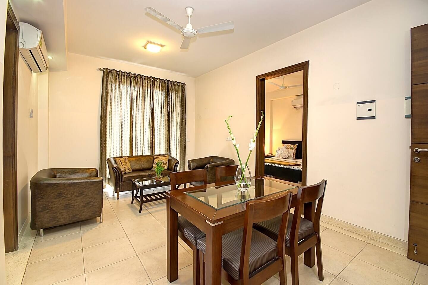 A hotel room with a dining area, a sofa, a chair, a table, a mirror, and an air conditioning unit.