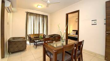 A hotel room with a dining area, a sofa, a chair, a table, a mirror, and an air conditioning unit.