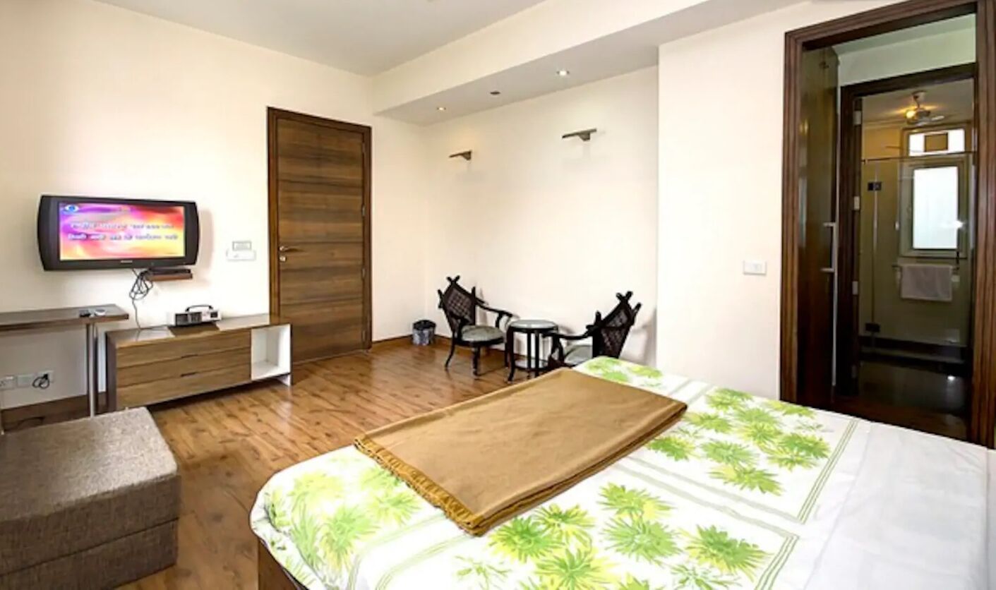 Habitación de hotel con cama, escritorio, televisor, silla y puerta.