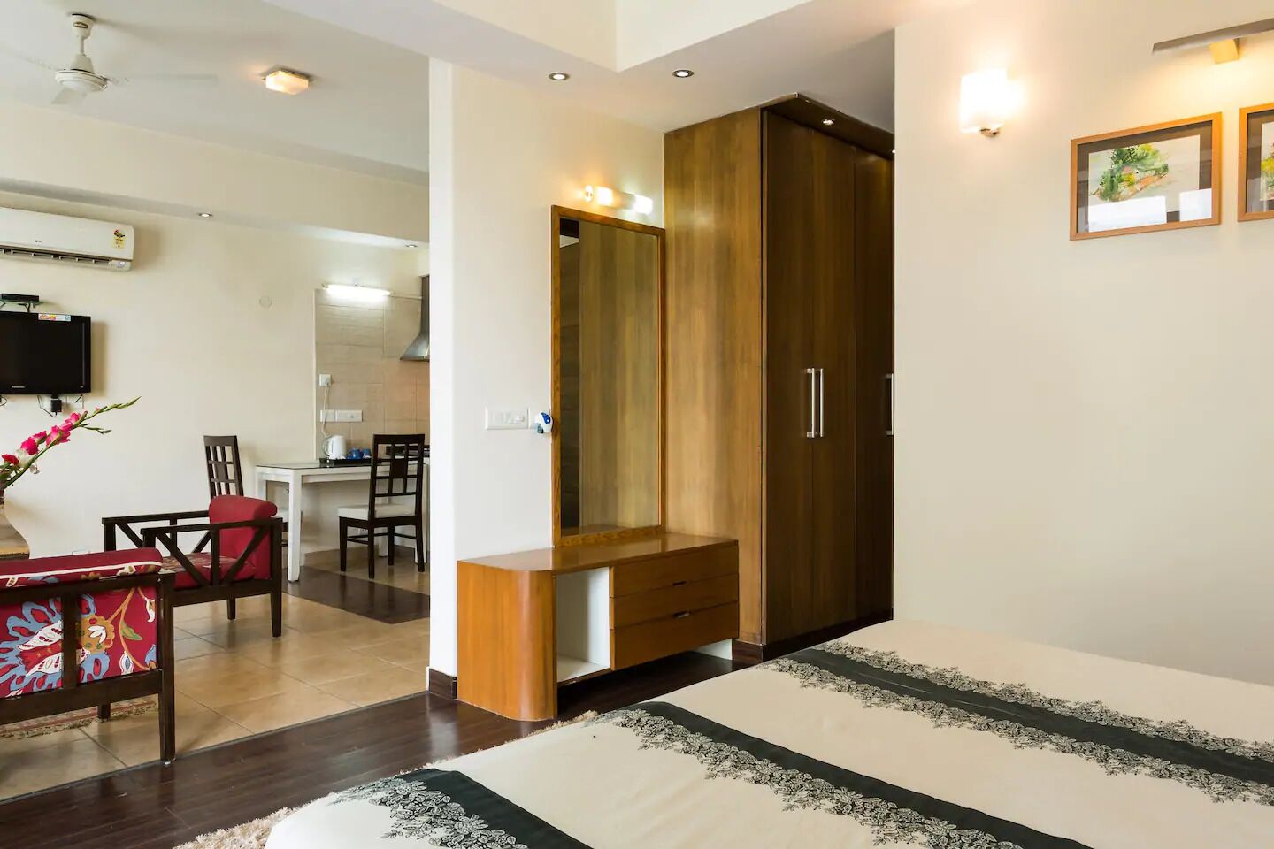 Un dormitorio con cama, un armario de madera, un escritorio con silla y un televisor montado en la pared.