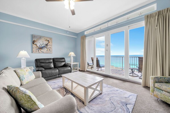 A living room with a sofa, coffee table, and a painting of a crab. There is a balcony with a view of the ocean.