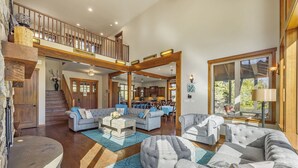 A spacious living area with a high ceiling, wooden beams, and a view to a kitchen and dining area. - Built for Time Together! Suncadia At It's Best | Greenside Spa + GameRm (Cle Elum)