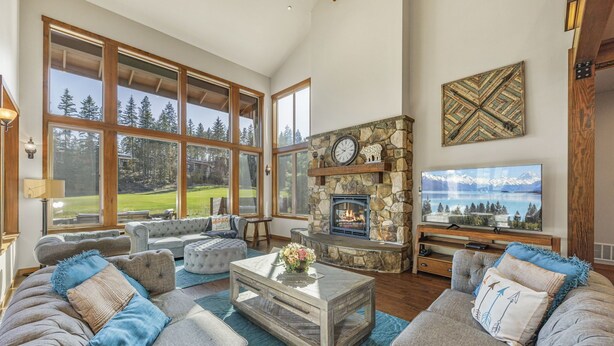 A spacious living room with a stone fireplace, large windows, and a television. - Built for Time Together! Suncadia At It's Best | Greenside Spa + GameRm (Cle Elum)