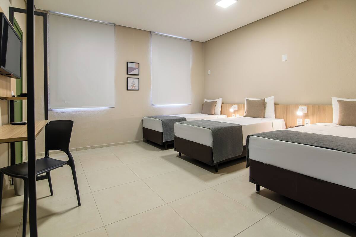 A hotel room with two single beds, a desk with a chair, and a TV on a stand.