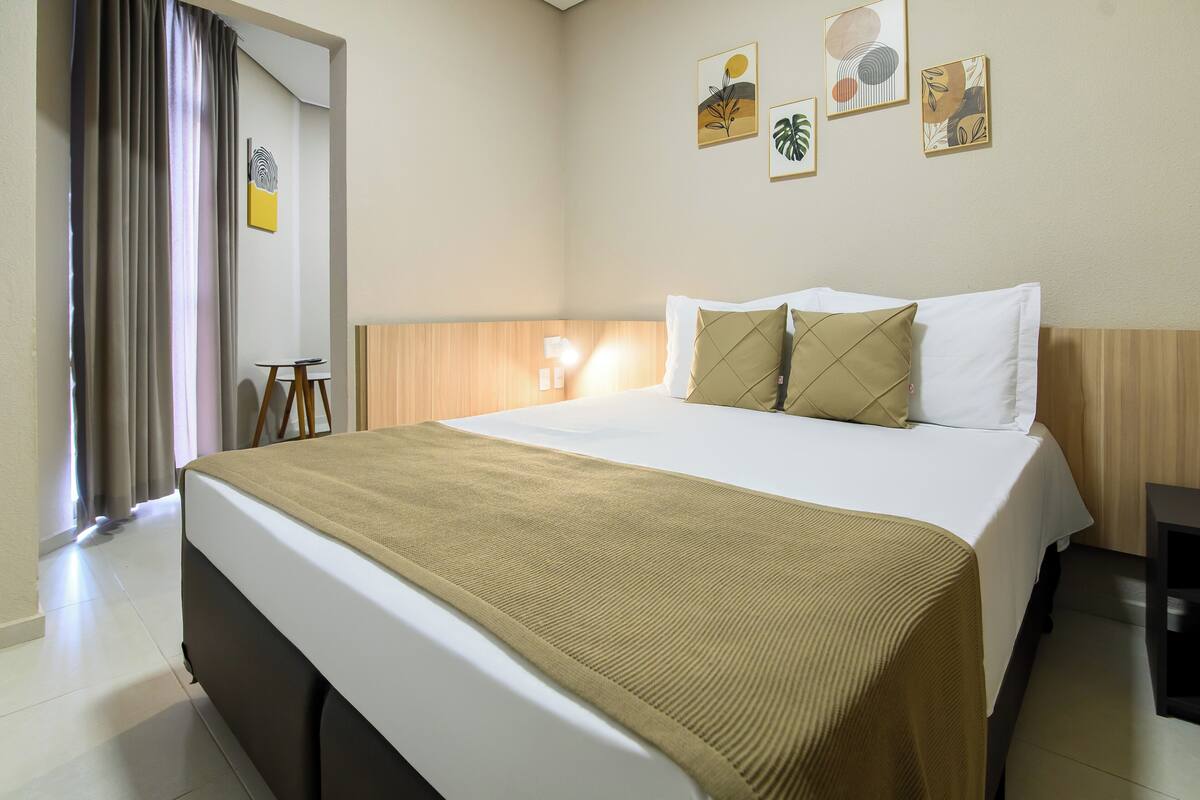 A hotel room with a bed, a bedside table, a lamp, and wall art.