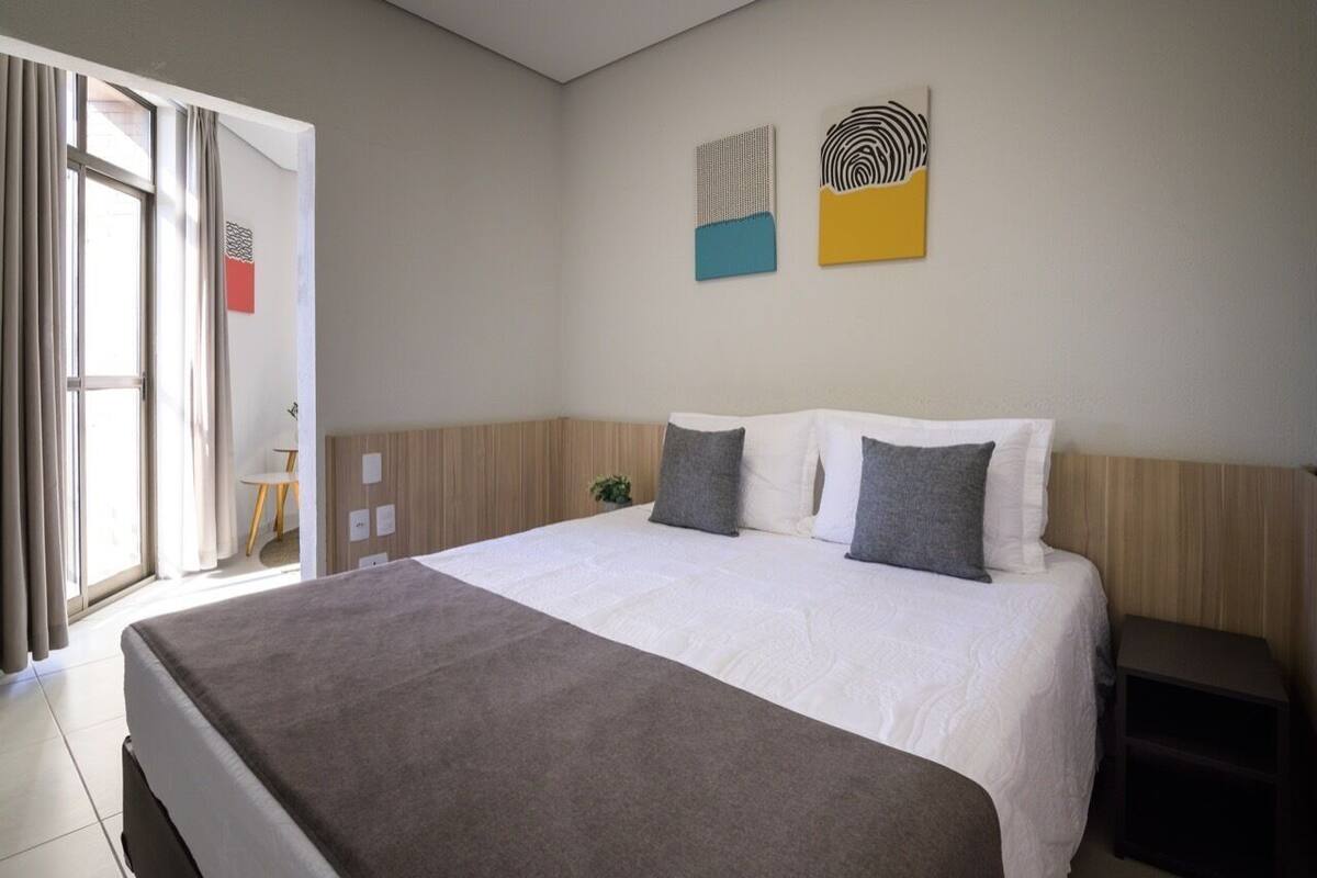 A hotel room with a bed, a bedside table, a window with curtains, and wall art.