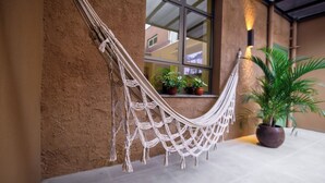 A hammock tied to a textured wall, a window with potted plants, and a potted palm tree. - Hotel Santa Cruz (Santa Cruz do Sul)