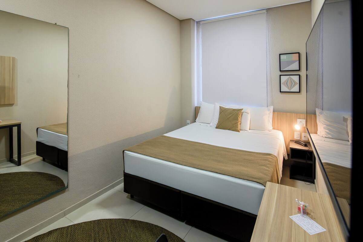 A hotel room with a bed, bedside table, and a mirror.
