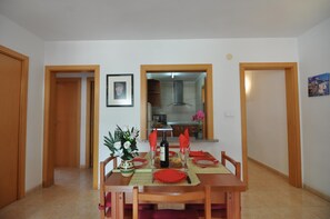 A dining area with a wooden table set for four, a vase with flowers, and a framed picture on the wall.