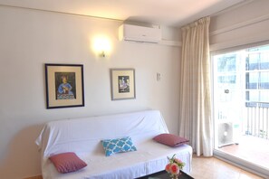 A white sofa with two pillows, a framed picture, and a wall-mounted air conditioner.