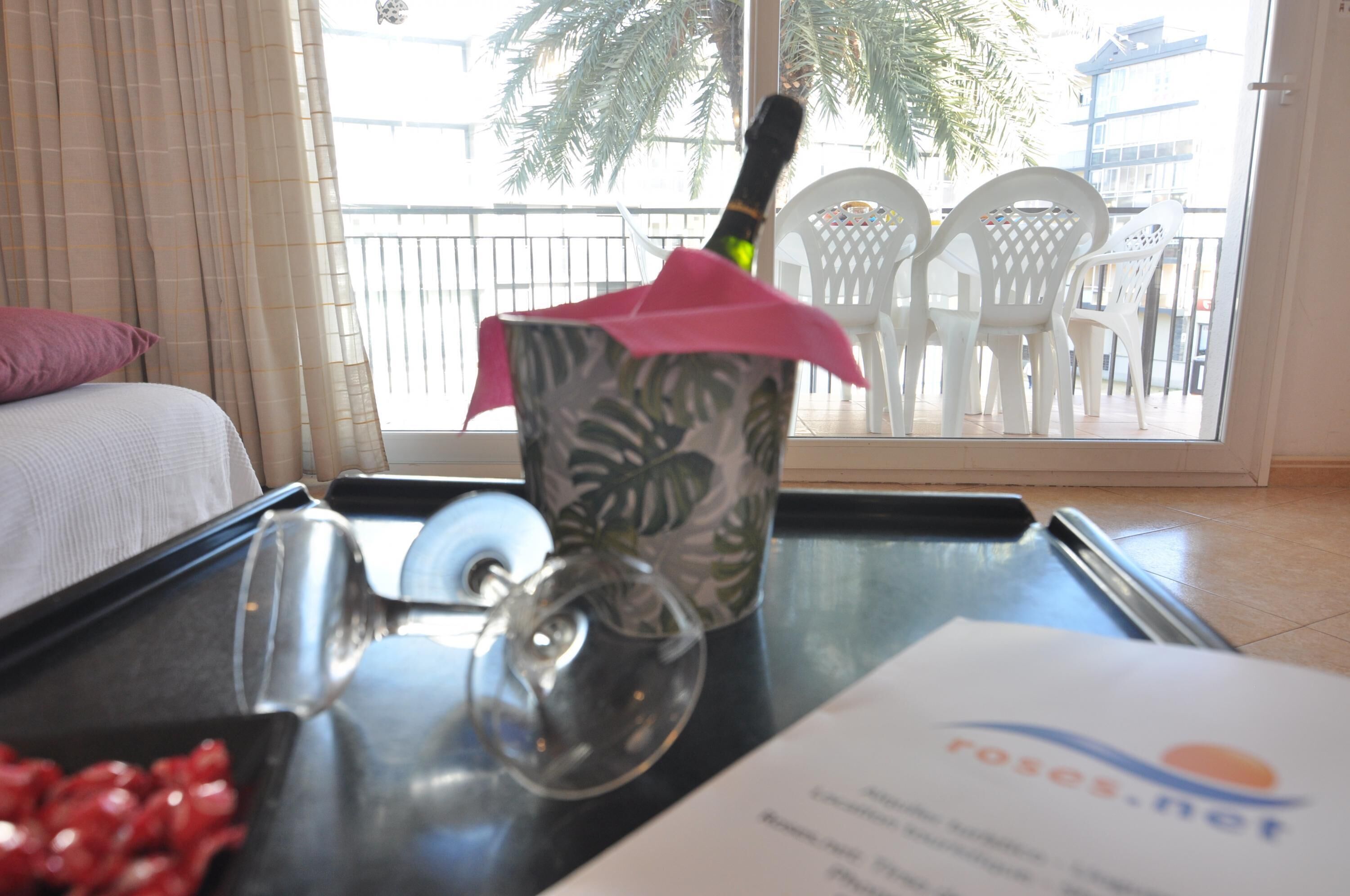A hotel room with a bed, a window with a view of palm trees, a table with a glass, a metal tray, and a piece of paper.