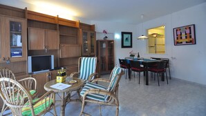 A dining area with wicker chairs, a round table, and a television on a stand. - Welcome to our cozy apartment for rent in Roses, Costa Brava! Just 300 meters from the beautiful Santa Margarita beach. (Roses)