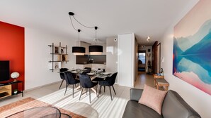A modern living room with a dining area, a flat-screen TV, and a large abstract painting. - Le Reposoir - New 2 bedroom apartment with terrace & garage (Annecy)