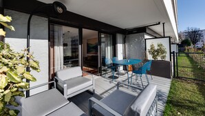 A modern outdoor patio with a glass door leading to an interior space, a small table with chairs, and a seating area with cushions. - Le Reposoir - New 2 bedroom apartment with terrace & garage (Annecy)