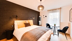 A modern hotel room with a large bed, bedside lamps, a small table with chairs, and a window with curtains. - Le Reposoir - New 2 bedroom apartment with terrace & garage (Annecy)