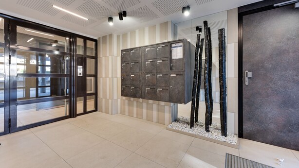 A modern lobby with a glass door entrance, a row of lockers, and a decorative plant arrangement. - Le Reposoir - New 2 bedroom apartment with terrace & garage (Annecy)