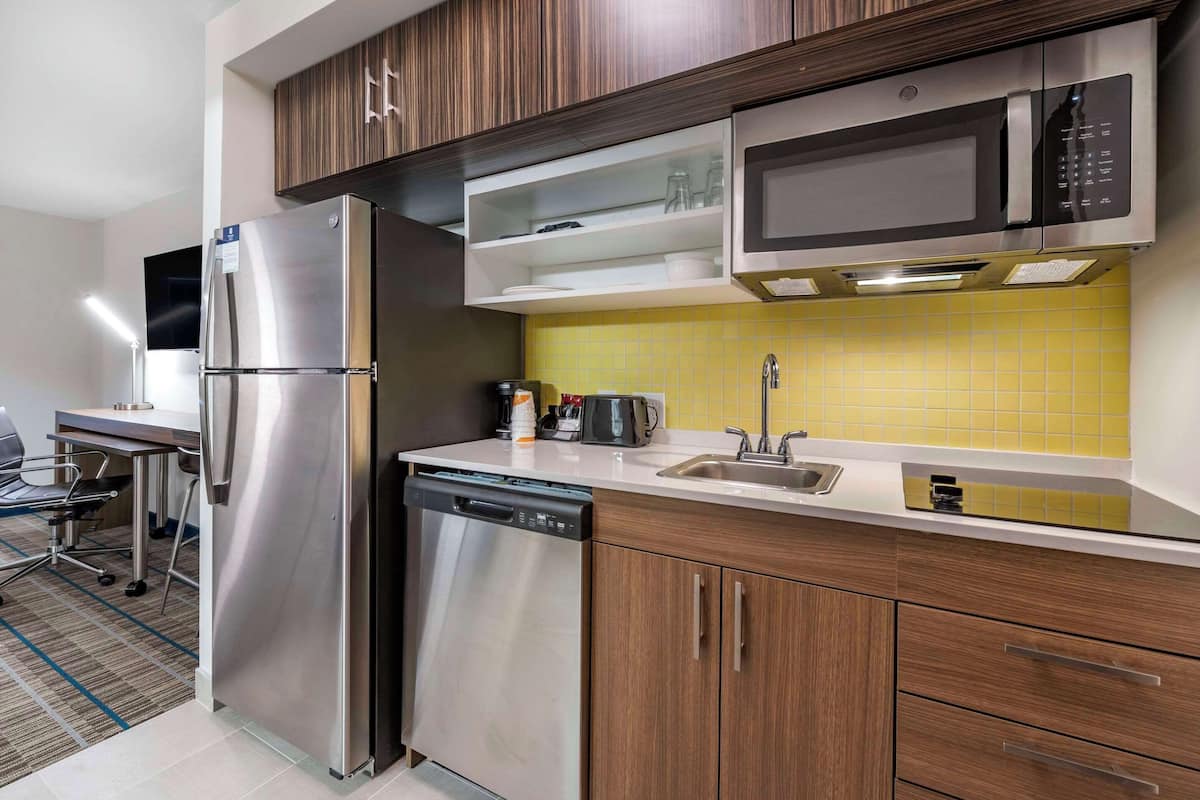 Una cucina moderna con elettrodomestici in acciaio inox, mobili impiallacciati in legno e zoccolo giallo in piastrelle.
