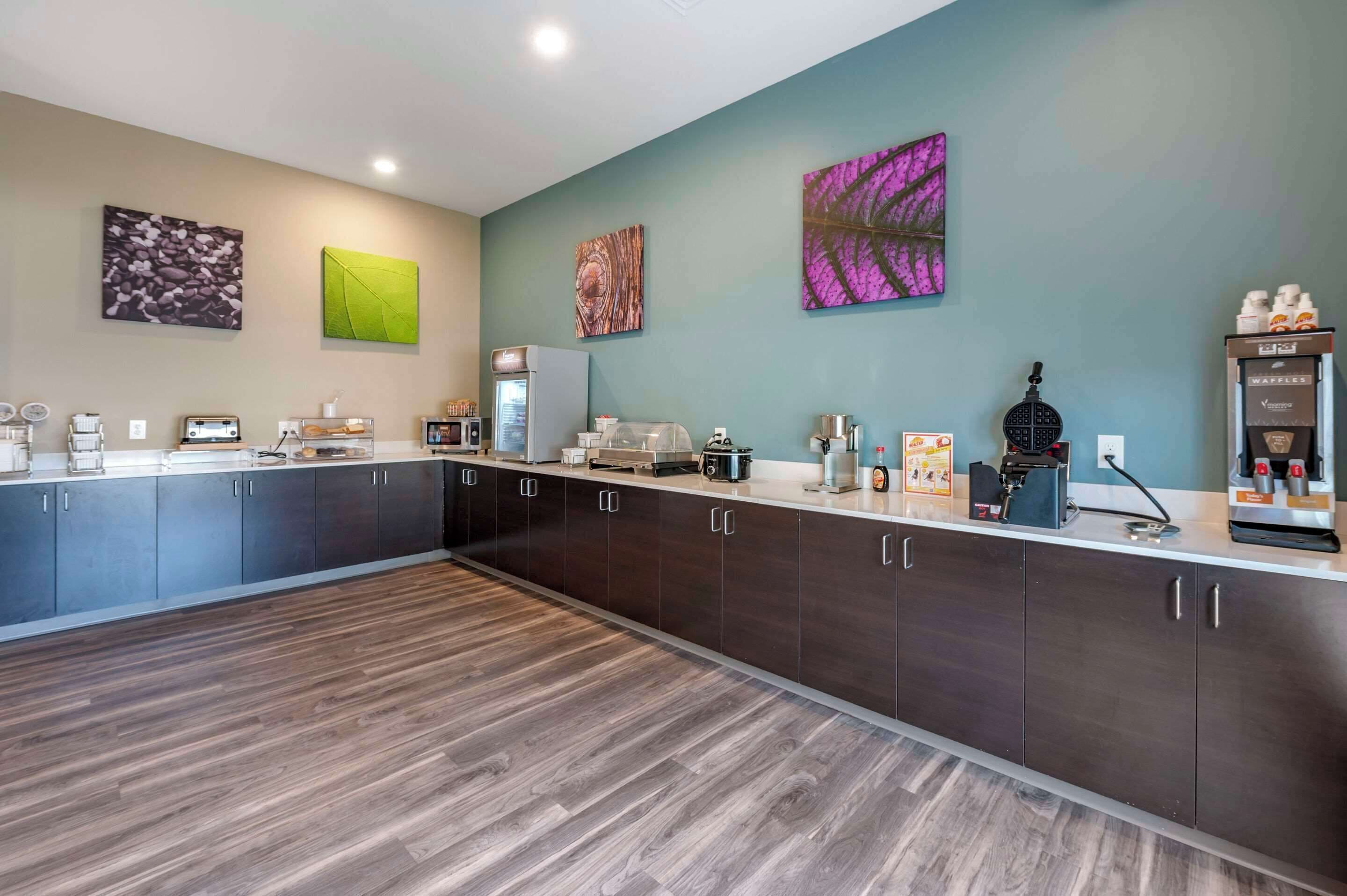 A modern kitchen with dark cabinets, a long countertop, and various appliances including a coffee machine and a waffle maker.