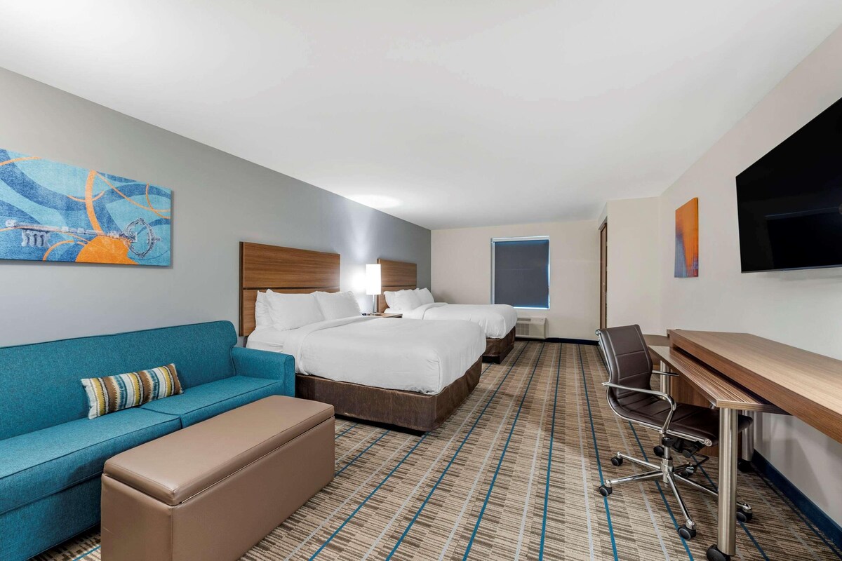 A hotel room with a sofa, two beds, a desk, and a TV.