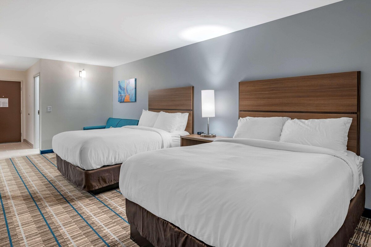 A hotel room with two beds, a blue accent wall, and a patterned rug.