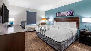 Une chambre d’hôtel avec un grand lit, un bureau avec un ordinateur, un téléviseur à écran plat et une fenêtre avec des stores.
