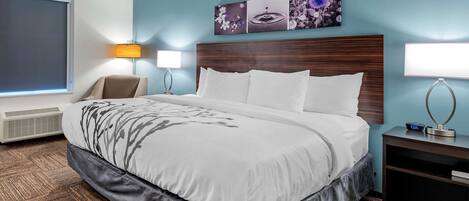 A hotel room with a large bed, two bedside lamps, a wall-mounted artwork, a window with blinds, and a heater.