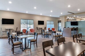 A modern dining area with tables and chairs, large windows, and a flat-screen TV mounted on the wall. - Sleep Inn (Georgetown)