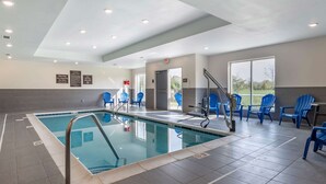 Une piscine intérieure avec des chaises bleues et un poste de surveillance pour le sauveteur, le tout entouré d’un sol et de murs carrelés, ainsi que de panneaux de signalisation de sécurité.