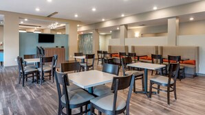 Un espace repas moderne doté de plusieurs tables et chaises, d’un téléviseur à écran plat fixé au mur et d’un panneau décoratif mural.