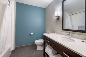 A bathroom with a blue wall, white toilet, and a vanity with a mirror and sink.