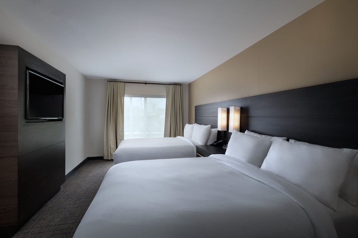 A hotel room with two beds, a TV, a nightstand, and a window with curtains.