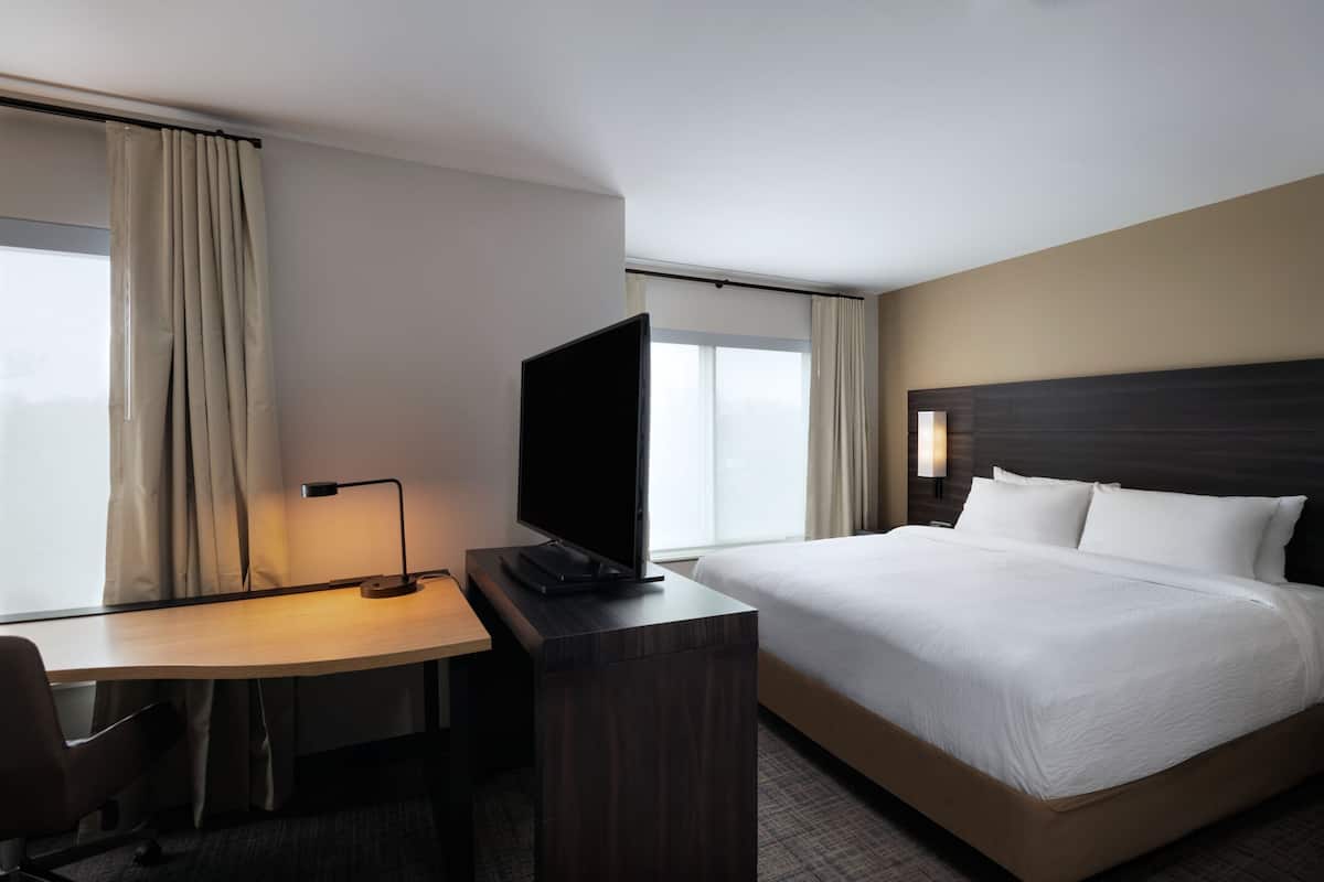 A hotel room with a bed, a desk with a television, a chair, and a window with curtains.