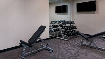A gym with benches, dumbbells, and a TV on the wall.