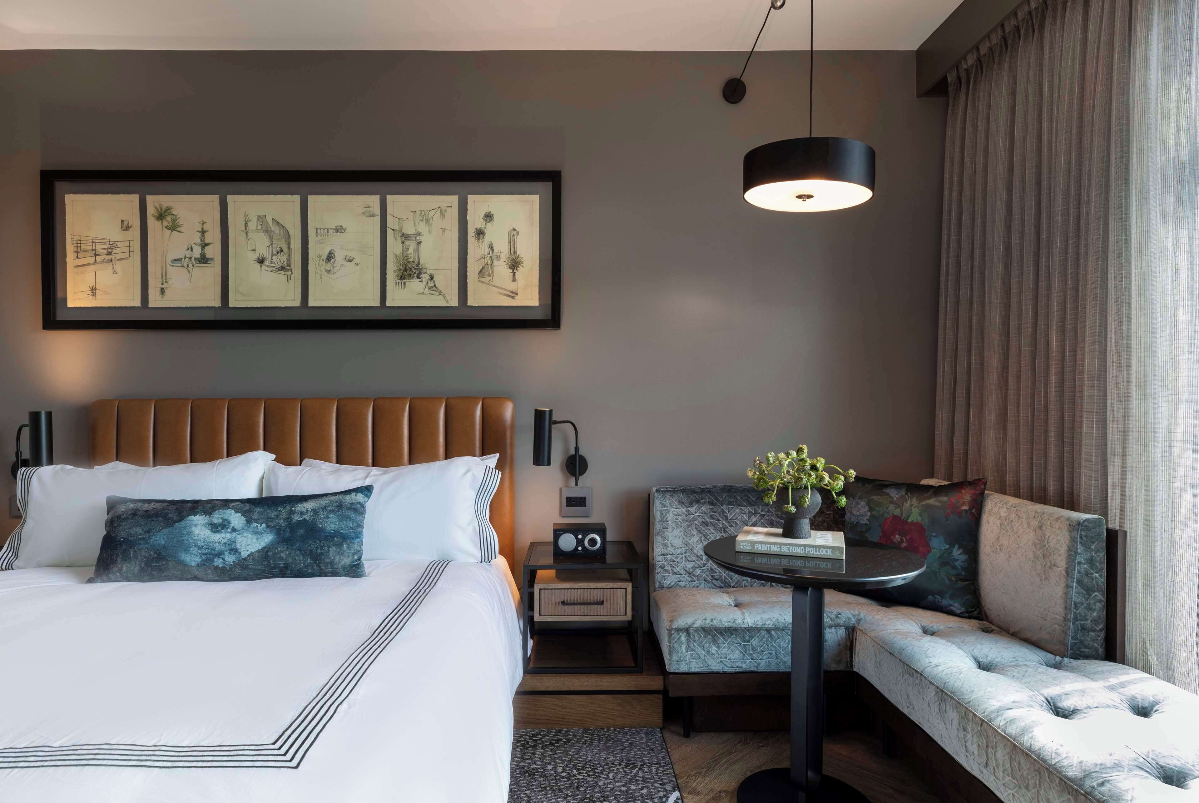 Ein modernes Hotelzimmer mit einem großen Bett, einer Couch, einem kleinen Tisch mit einer Vase und einem gerahmten Kunstwerk über dem Bett.