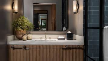 A modern bathroom with a large mirror, two wall-mounted lights, a wooden vanity, and a geometric patterned floor.