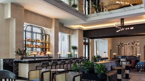 Un moderno hall de hotel con zona de bar, diferentes disposiciones de asientos y un alto techo con luminarias.
