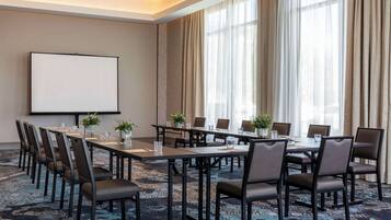 A conference room with a large table, chairs, a projector screen, and large windows with curtains.