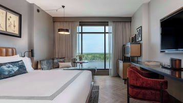 Habitación de hotel con una cama grande, un escritorio con silla, televisión y vistas al exterior.