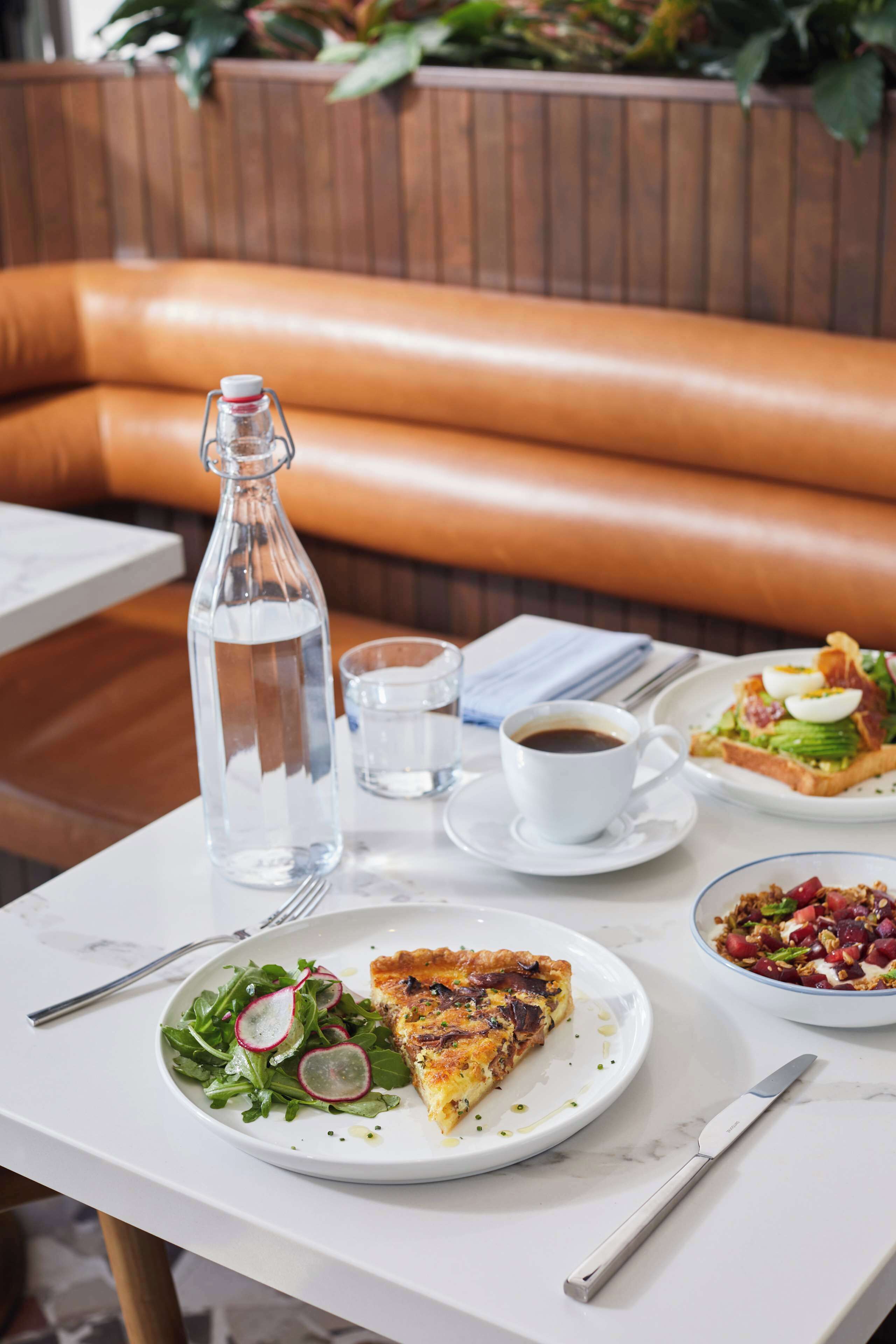 A dining table with a bottle of water, a cup of coffee, a plate with a slice of pizza, a bowl of salad, and a knife.
