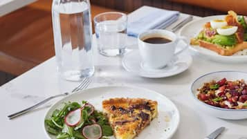 A dining table with a bottle of water, a cup of coffee, a plate with a slice of pizza, a bowl of salad, and a knife.
