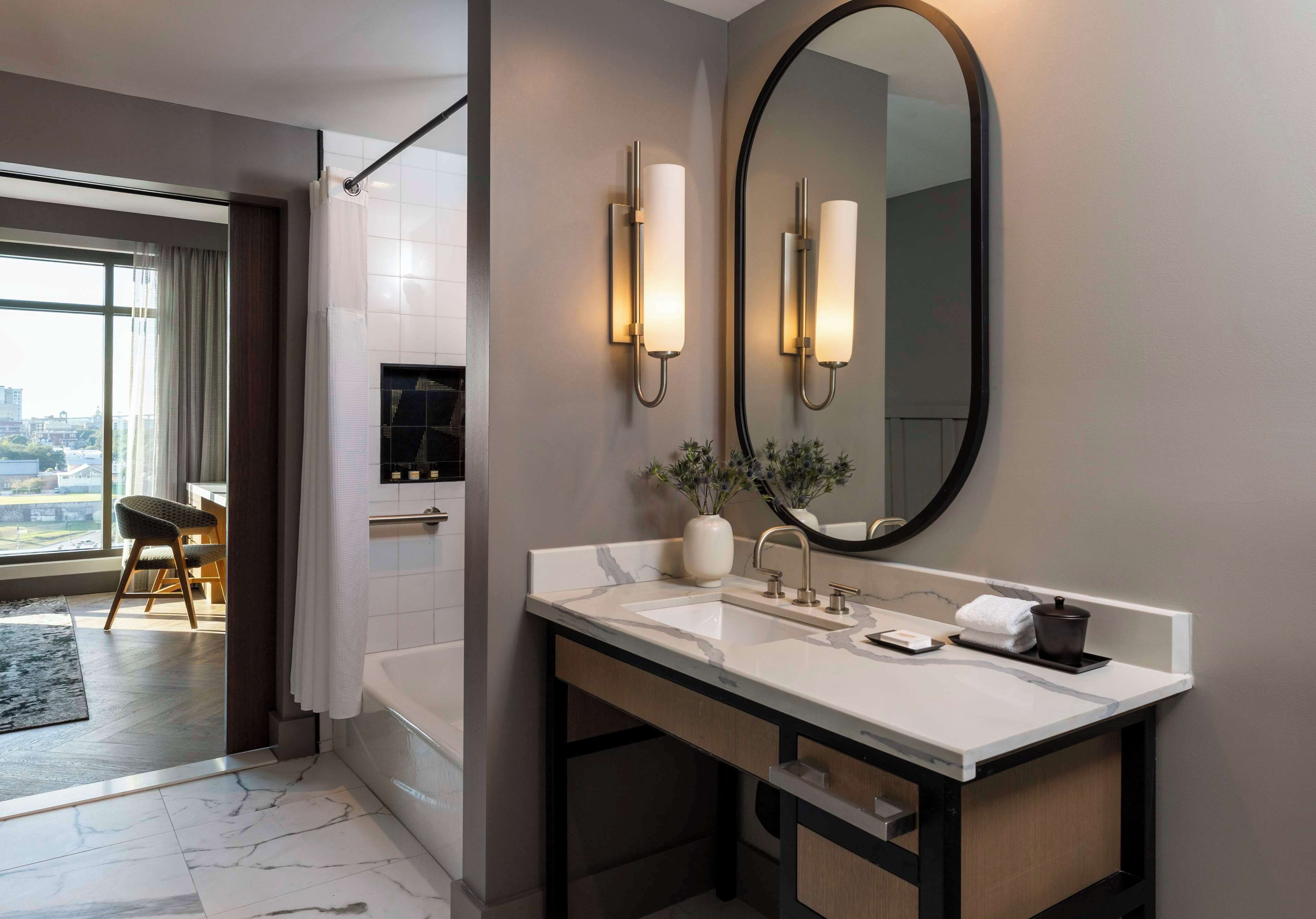 A modern bathroom with a large mirror, two wall-mounted lights, a marble sink, and a bathtub.