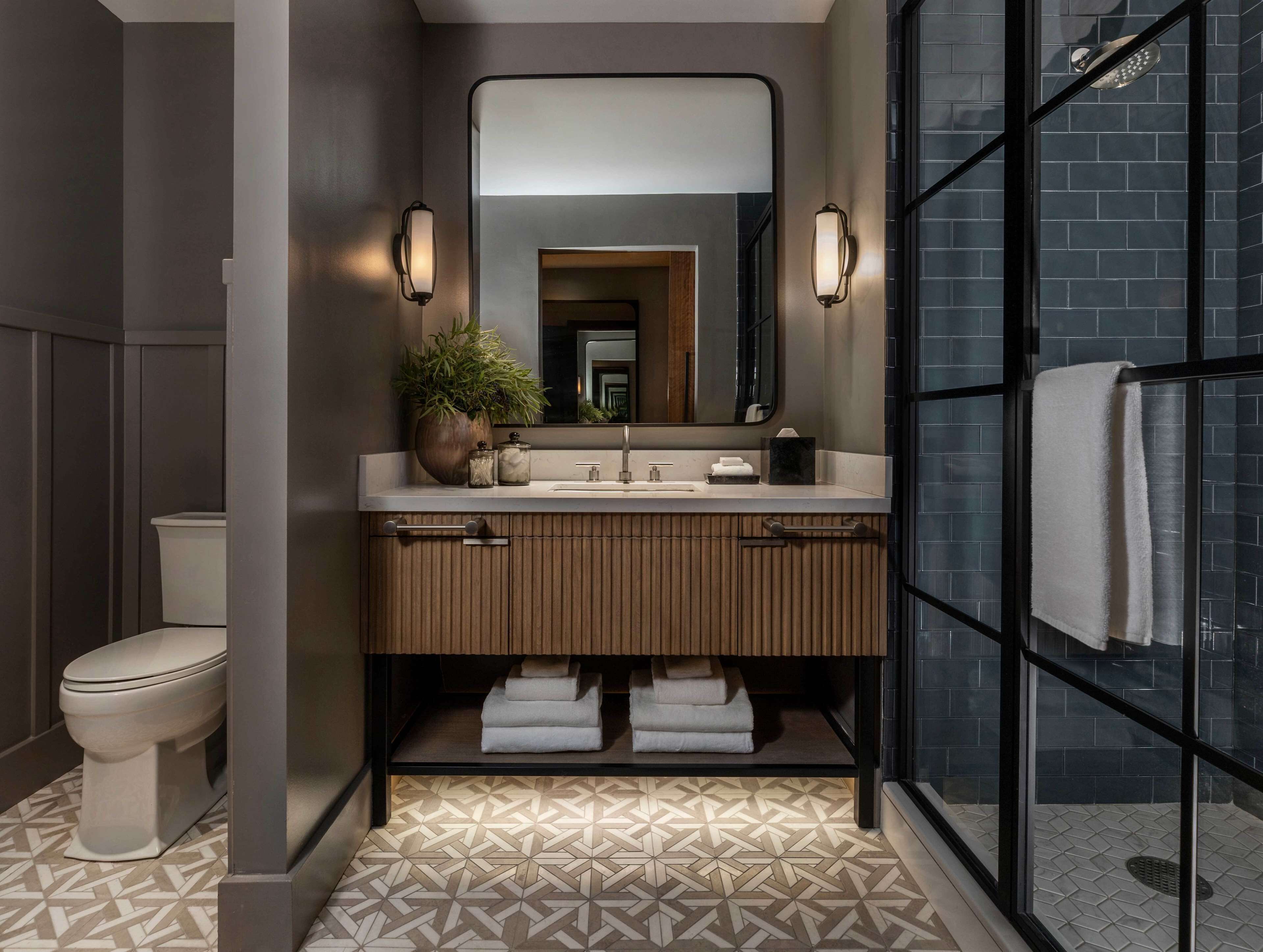 Une salle de bain moderne avec un meuble-lavabo, un évier et un miroir. Les toilettes se trouvent à gauche et l’espace douche à droite.