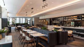 Un restaurante moderno con una barra alargada, varias mesas para comer y una cocina visible al fondo.