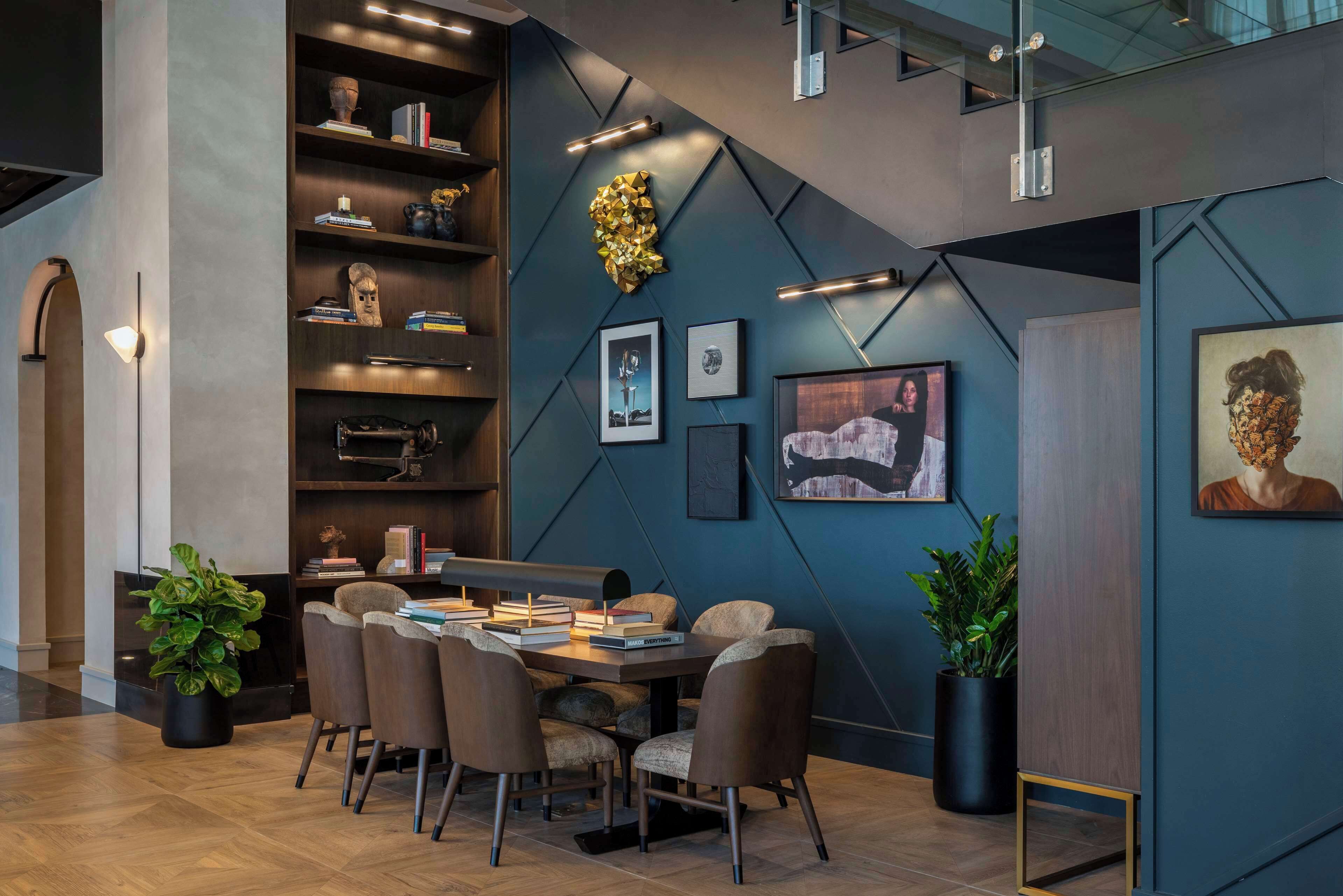 A modern conference room with a round table, six chairs, and a bookshelf filled with books and decorative items.
