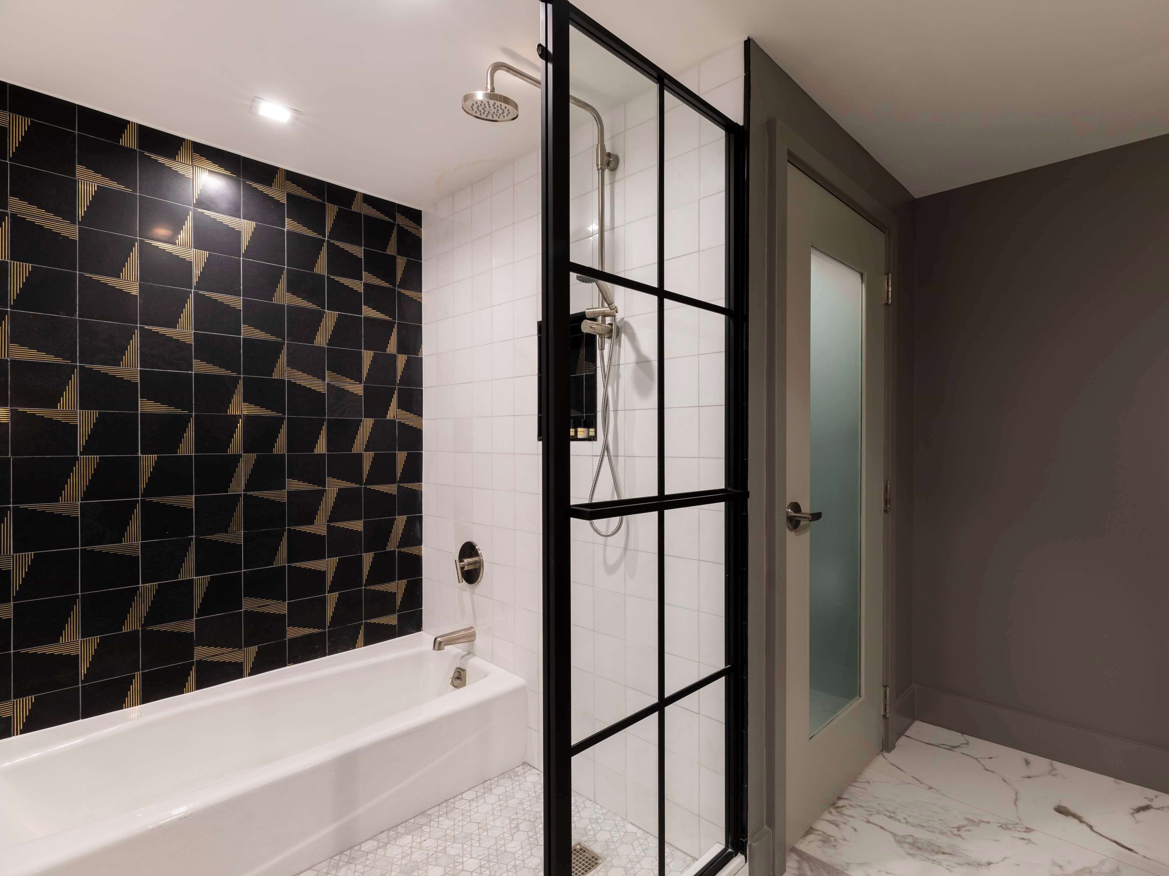A modern bathroom with a black and white tiled wall, a white bathtub, and a glass-enclosed shower area.