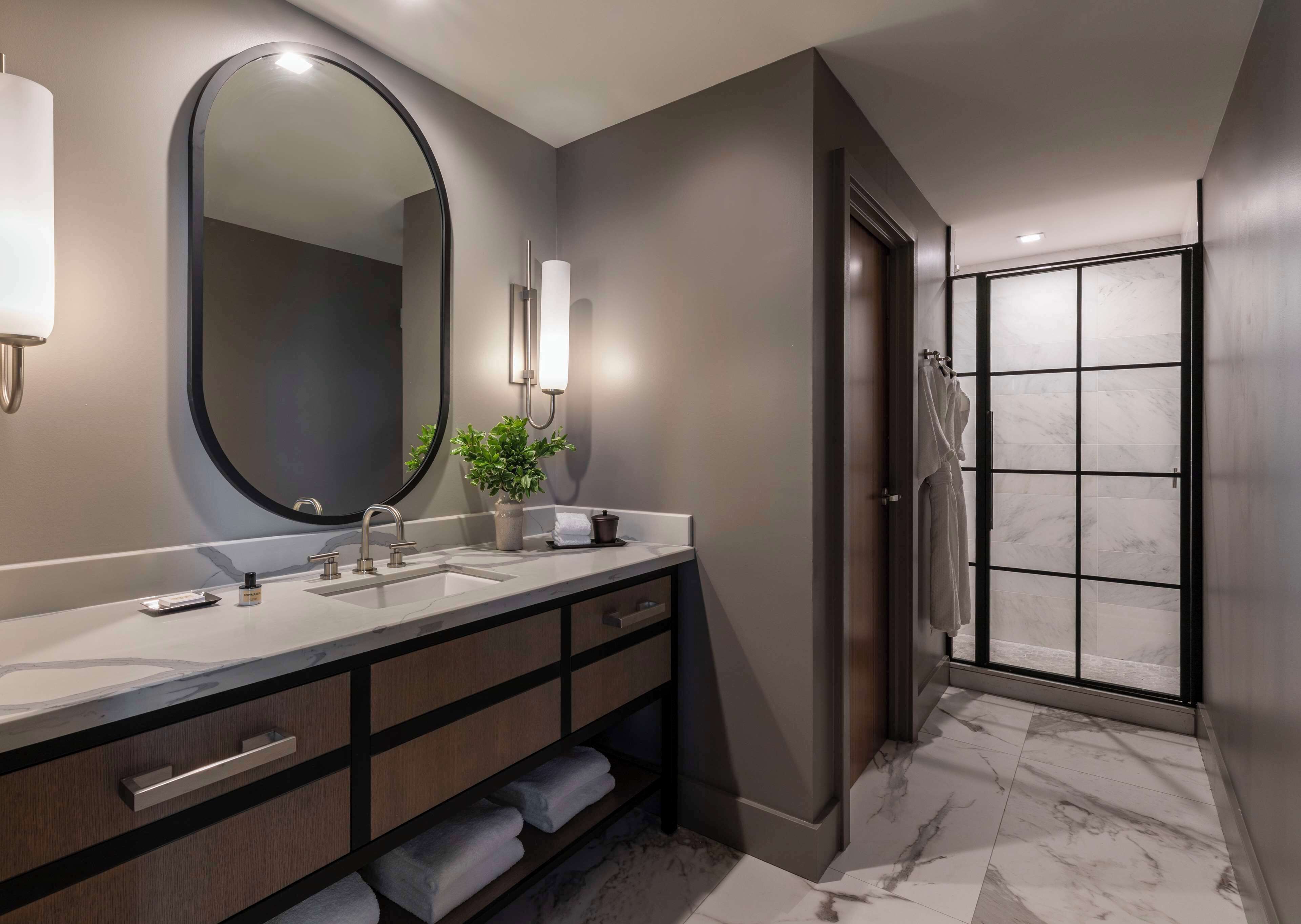 A modern bathroom with a large mirror, a sink, a towel rack, and a shower area.