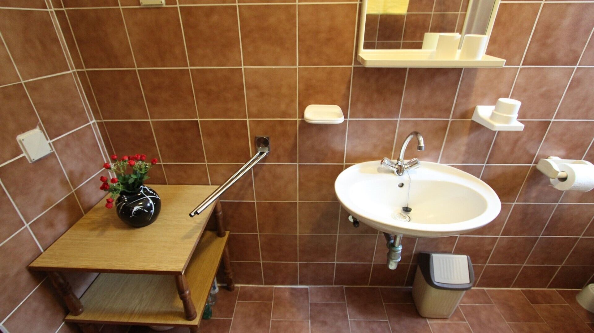 A bathroom with a wooden vanity, a sink, a mirror, and a trash bin.