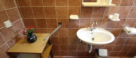 A bathroom with a wooden vanity, a sink, a mirror, and a trash bin.