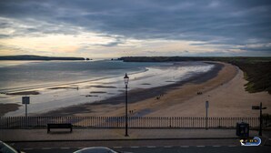 A beach with a paved walkway, benches, and a lamppost. - 2 South Beach Court - Beach Apartment (Tenby)